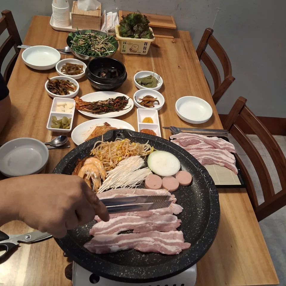 불판 위에서 맛있게 익어가는 생삼겹살과 다양한 곁들임 채소