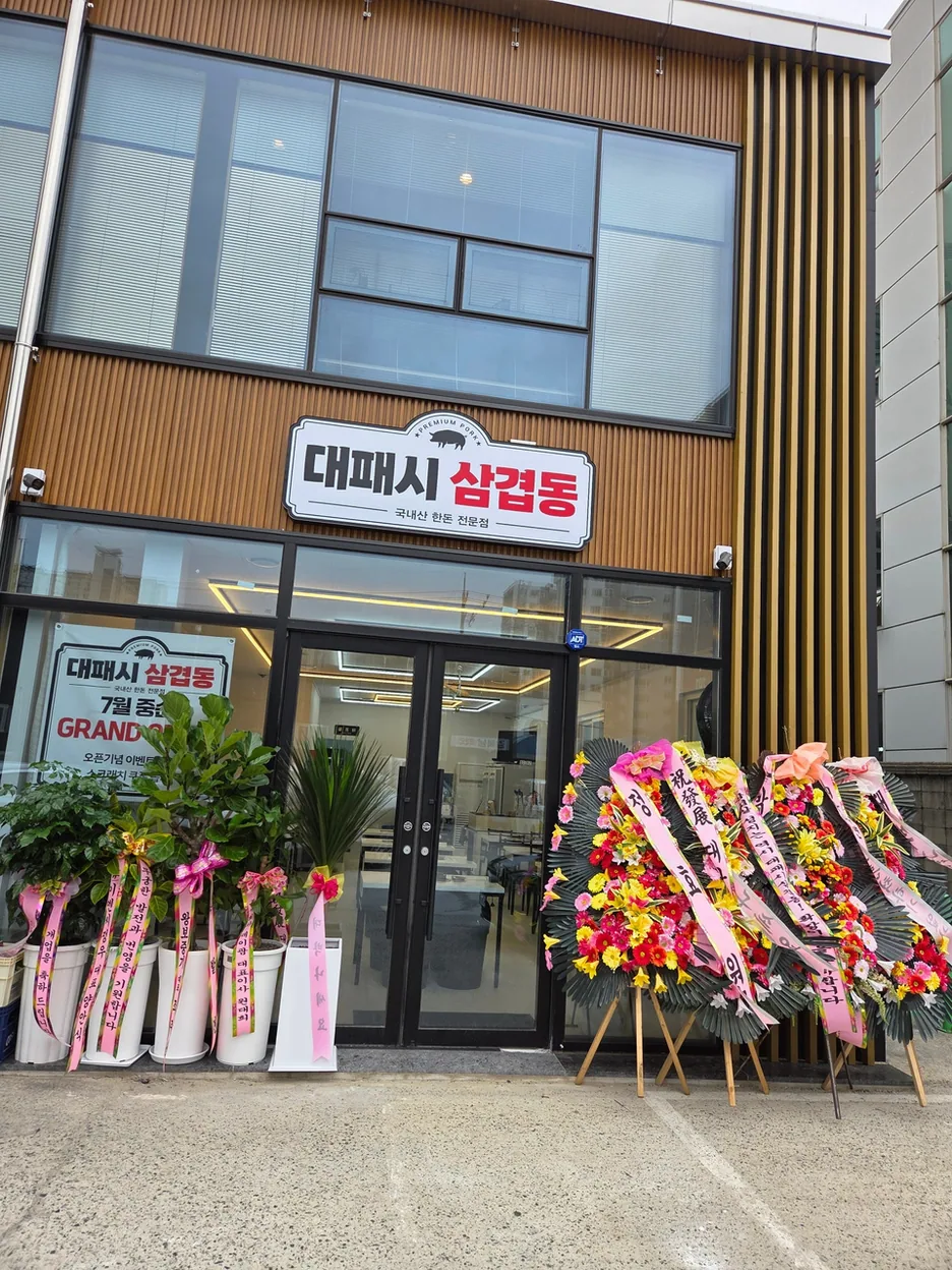 매장 입구에 놓인 화환들과 세련된 간판이 있는 대패시삼겹동 외관